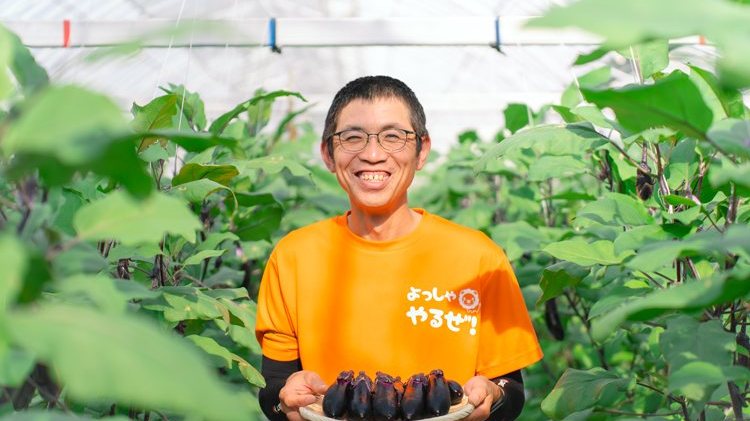 収穫したナスを手にする園主